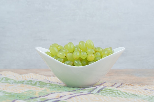Fresh grapes in white bowl on tablecloth. 