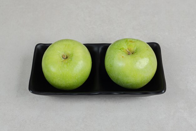 Свежие зеленые яблоки на черной тарелке