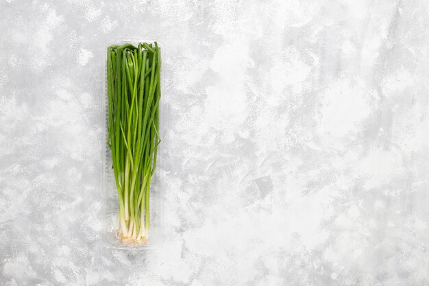 Fresh green onions in plastic box on grey concrete