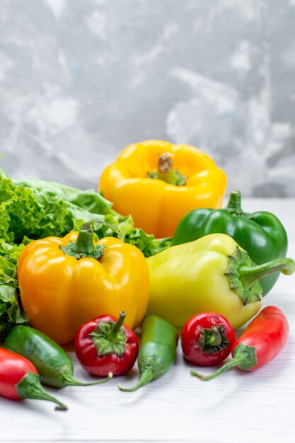 fresh green salad along with colored bell peppers and spicy peppers on light desk