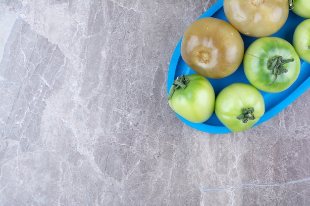 Fresh green tomatoes and pickled tomatoes on blue plate.