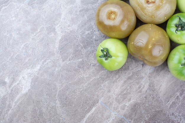 Свежие зеленые помидоры и маринованные помидоры на мраморной поверхности.