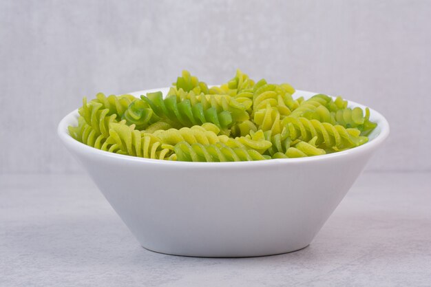 Свежие зеленые сырые спиральные макароны на белой тарелке
