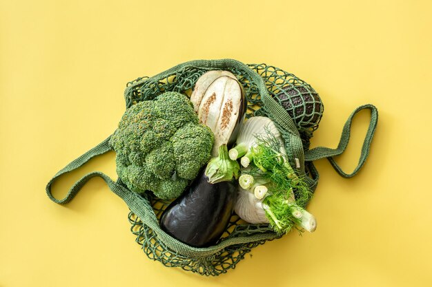 노란색 배경의 평평한 자루에 있는 녹색 끈 가방에 신선한 녹색 야채