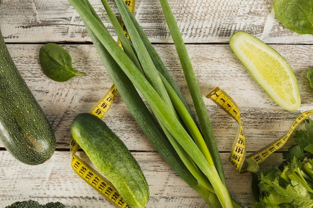 Fresh green vegetables with measuring tape on wooden backdrop