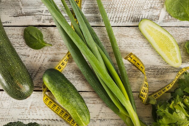 Fresh green vegetables with measuring tape on wooden backdrop