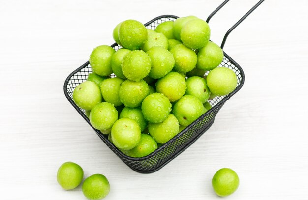 Свежие greengages в черном дуршлаге на белой деревянной планке. высокий угол обзора.