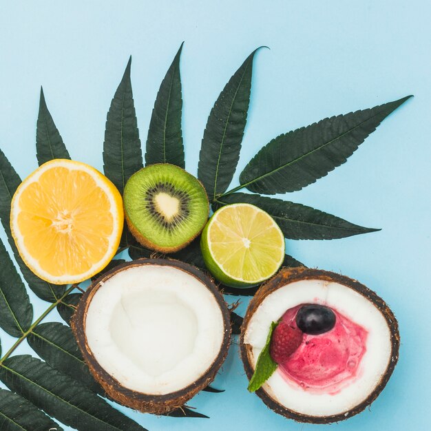 Fresh halved orange; kiwi; lemon and coconut with ice cream on green leaves against blue backdrop