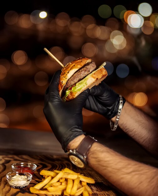Свежий гамбургер в черных перчатках