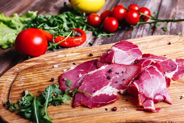 Свежая и полезная еда. Нарезанное красное мясо лежит на деревянном столе с рукколой