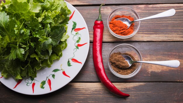 Fresh herbs on plate near pepper in bowls and chili