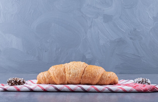 Fresh homemade croissant and pine cone over grey background.