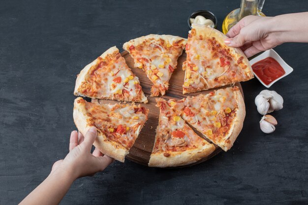 新鮮な自家製のおいしいピザ。黒いテーブルの上にピザのスライスを取る女性の手。