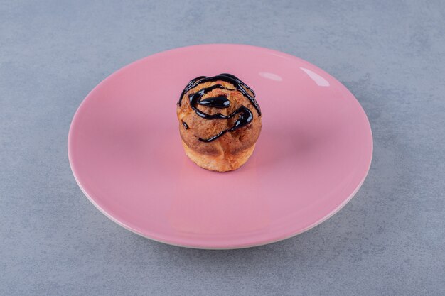 Fresh homemade muffin with chocolate slice on pink plate over grey surface