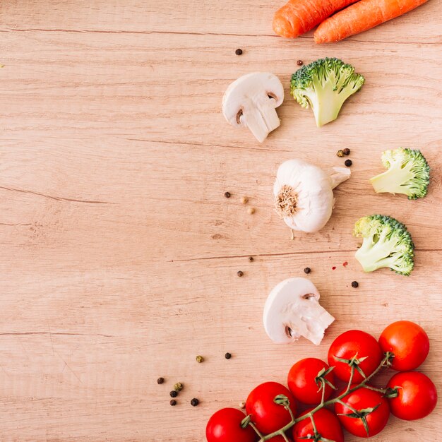 Fresh ingredients black pepper; mushroom; cherry tomatoes; garlic bulb and carrot on wooden surface