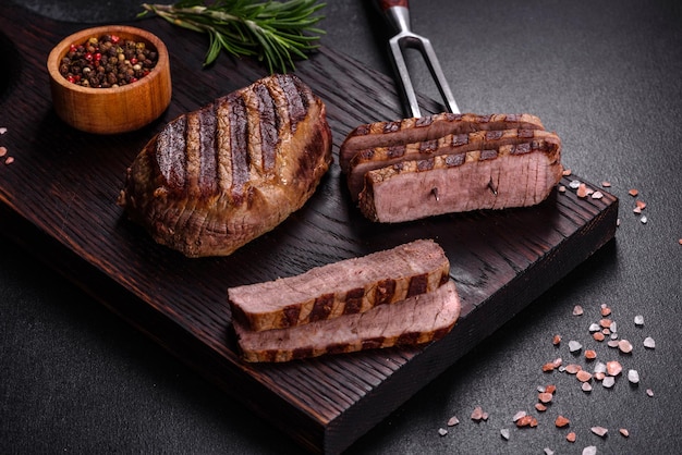 어두운 배경에 신선한 육즙이 맛있는 쇠고기 스테이크. 향신료와 허브를 곁들인 고기 요리