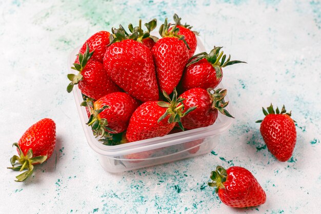 Fresh juicy strawberries in plastic lunch box on light