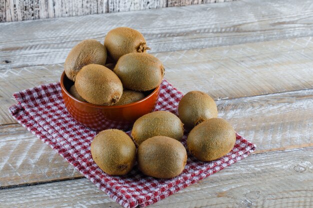 Fresh kiwi in a bowl on wooden and picnic cloth. high angle view.