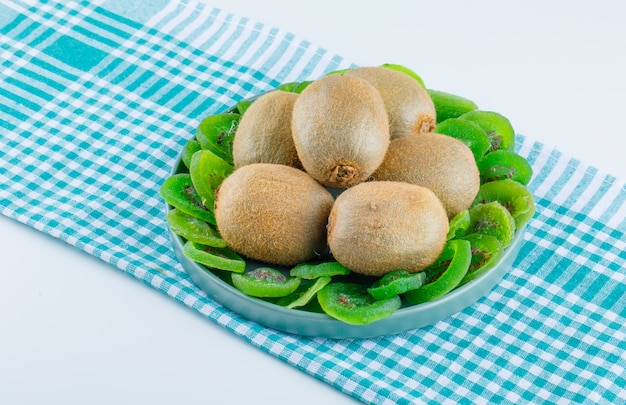 Fresh kiwi in a plate with dried kiwi high angle view on white and picnic cloth background