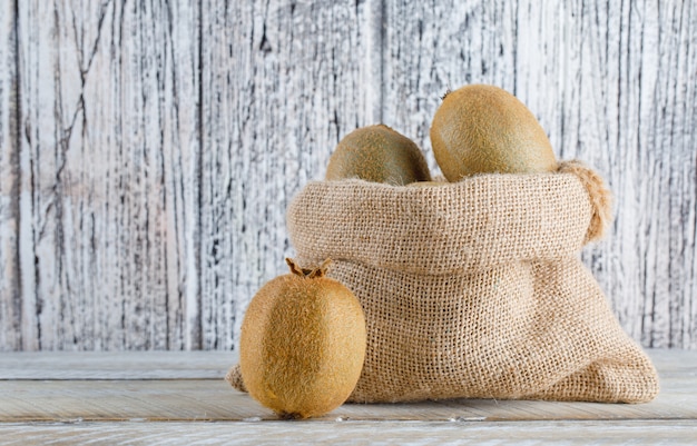 Fresh kiwi in a sack on a wooden table. side view.