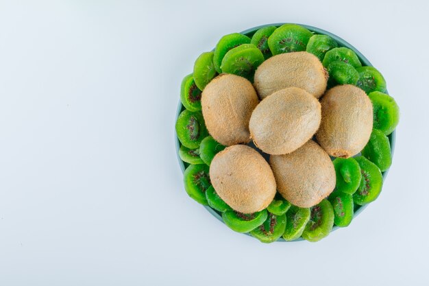 Fresh kiwi with dried kiwi in a plate on white background, flat lay.