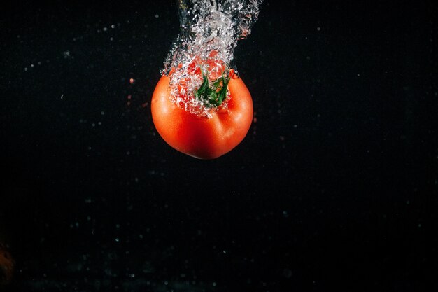 Fresh large tomato falls in water and makes bubbles