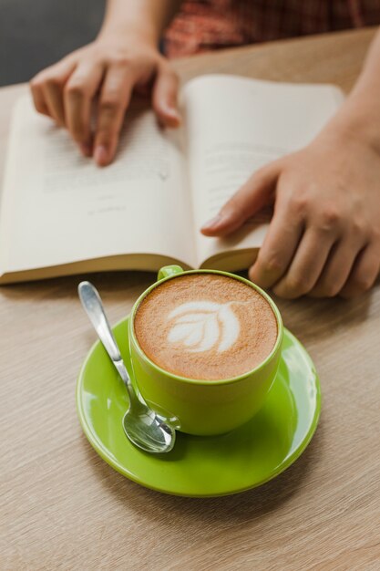 机の上の本を読んでいる人の近くのラテアートと新鮮なラテコーヒー