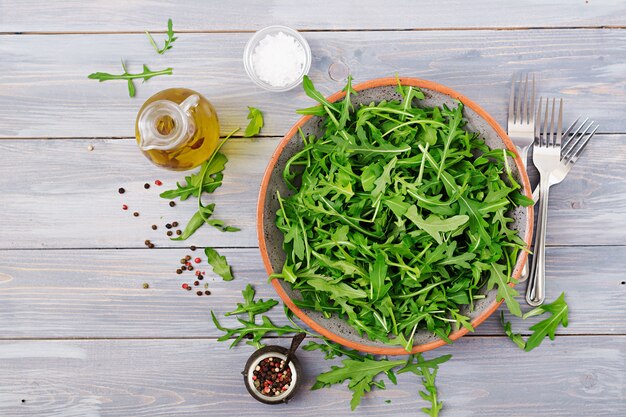 Fresh leaves of arugula in a bowl on a light wooden background. Flat lay. Top view