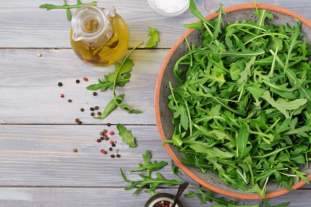 Fresh leaves of arugula in a bowl on a light wooden background. Flat lay. Top view