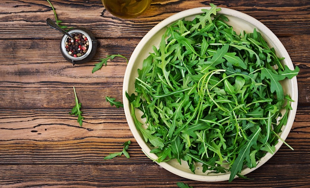 Fresh leaves of arugula in a bowl on a wooden background. Flat lay. Top view