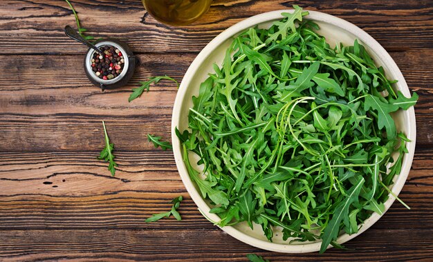 Fresh leaves of arugula in a bowl on a wooden background. Flat lay. Top view