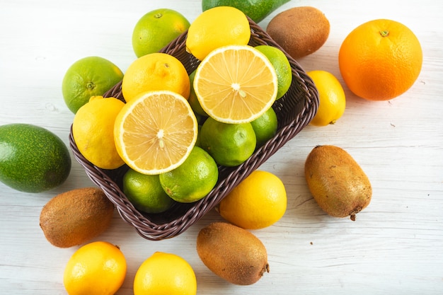 Fresh lemons in basket surrounded with citrus fruits on white wooden 
