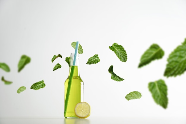 Fresh lime herbal drink inside transparent cocktail opened bottle with blue drinking straw inside