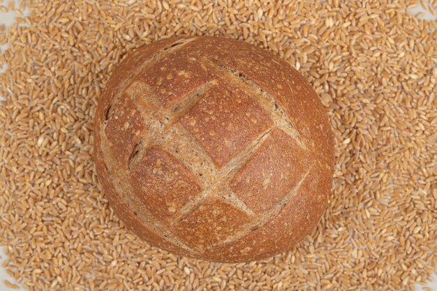 Fresh loaf of bread with oat grains on white surface