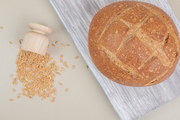 Fresh loaf of bread with oat grains on white surface