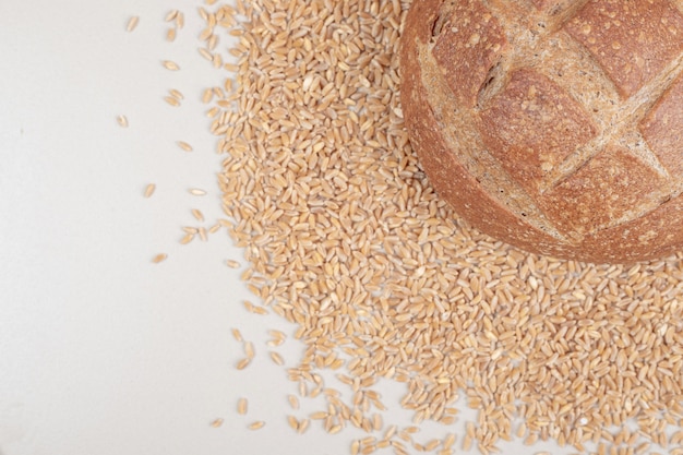 Fresh loaf of bread with oat grains on white surface