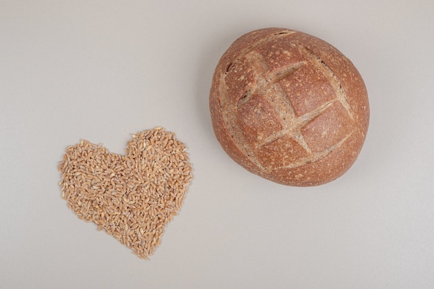 Fresh loaf of bread with oat grains on white surface