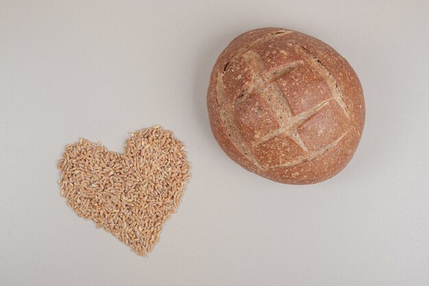 Fresh loaf of bread with oat grains on white surface