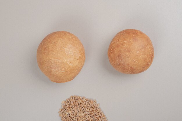 Fresh loaf of bread with oat grains on white surface