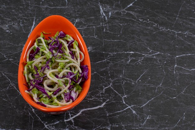 Fresh made spaghetti with vegetable sauce in orange bowl.