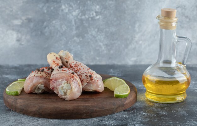 Fresh marinated chicken drumstick with lime and oil over grey background.