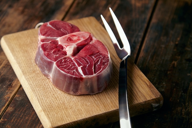 Стейк из свежего мяса с косточкой на деревянной тарелке с большой вилкой