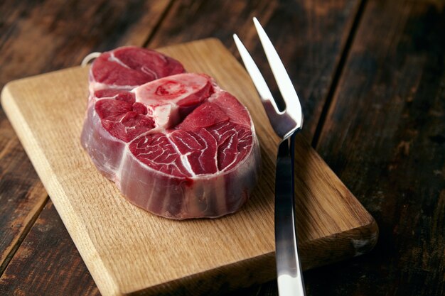 大きなフォークで木のプレートに骨付きの新鮮な肉ステーキ