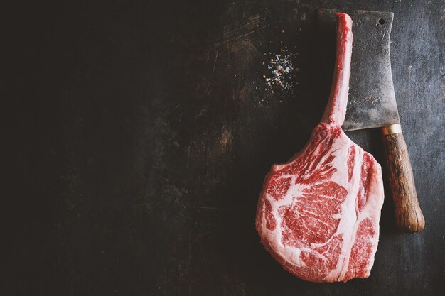 Fresh meat tomahawk steak on old wooden board. Dark background. Closeup