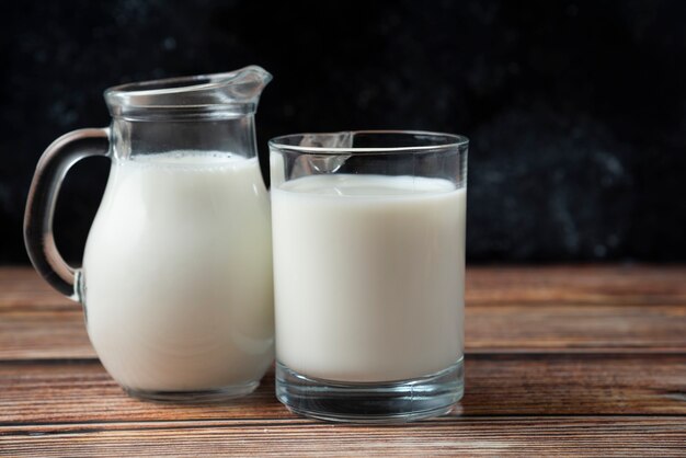 Fresh milk in a mug and jug on wooden table. 