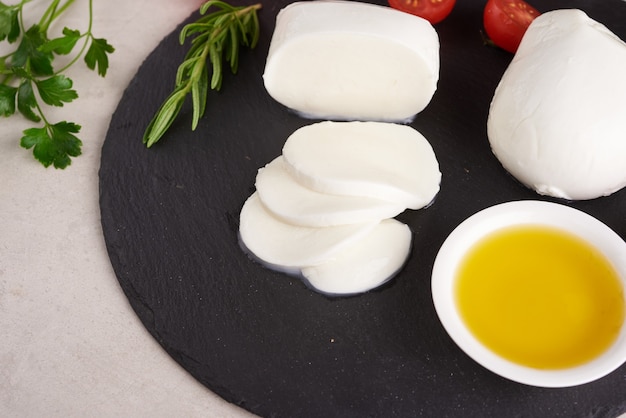 Fresh mozzarella cheese, Soft italian cheeses, tomato and basil, olives oil and rosemary on wooden serving board over light wooden surface. Healthy food. Top view. Flat lay.