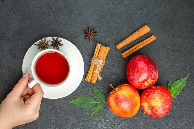 Fresh natural organic red apples with green leaves cinnamon limes and a cup of tea on black background