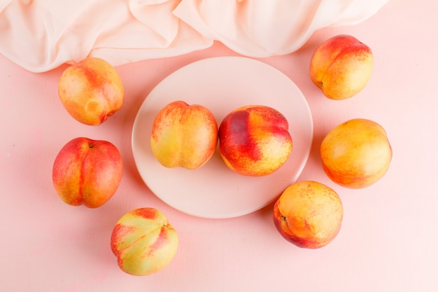 Fresh nectarines in a plate flat lay on pink and textile table