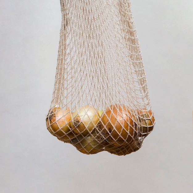 Fresh onions in the hanging white net against grey wall