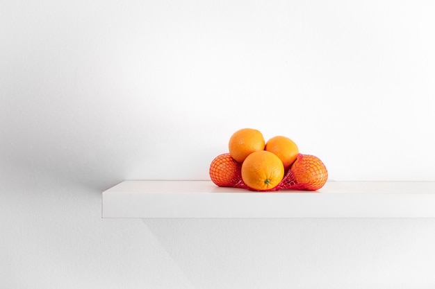 Свежие апельсины в сетке на полке на белом фоне